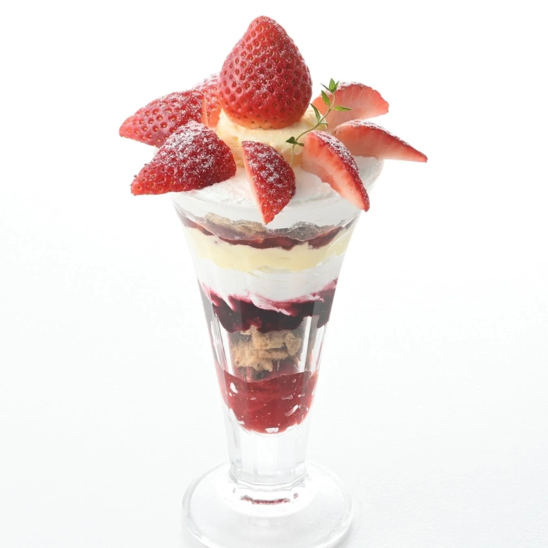 A beautifully crafted strawberry parfait with whipped cream, custard, and berry sauce, topped with powdered sugar.