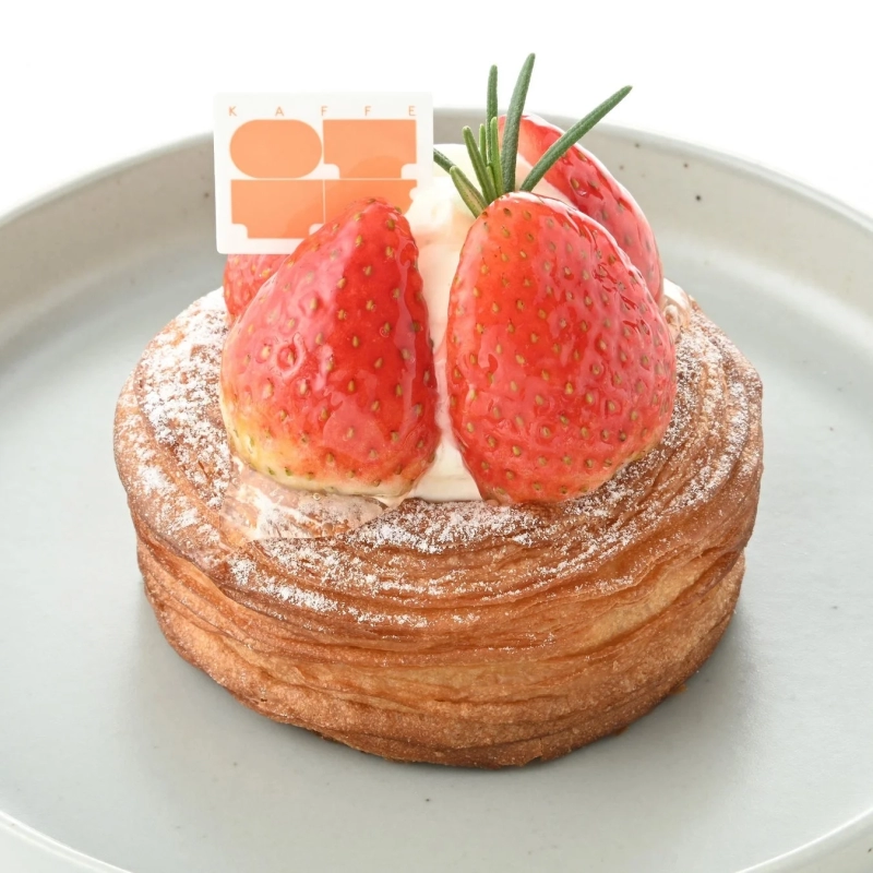 A round Danish pastry topped with fresh strawberries, whipped cream, and rosemary, dusted with powdered sugar.