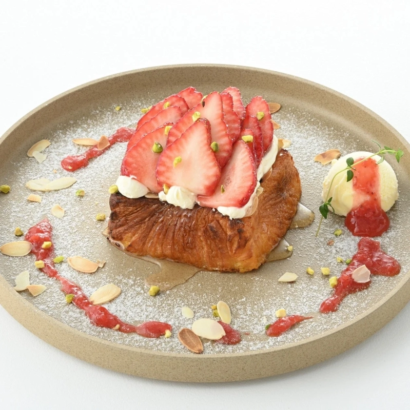 A fluffy Danish French toast adorned with fresh strawberries, cream, and nuts, dusted with powdered sugar.