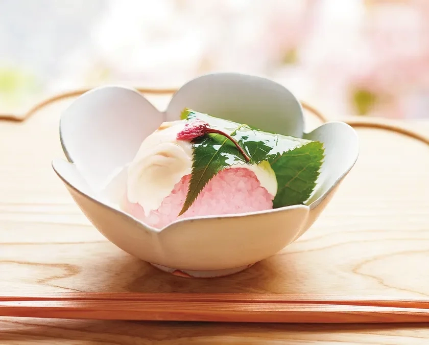 A pink wagashi adorned with a cherry blossom and leaf