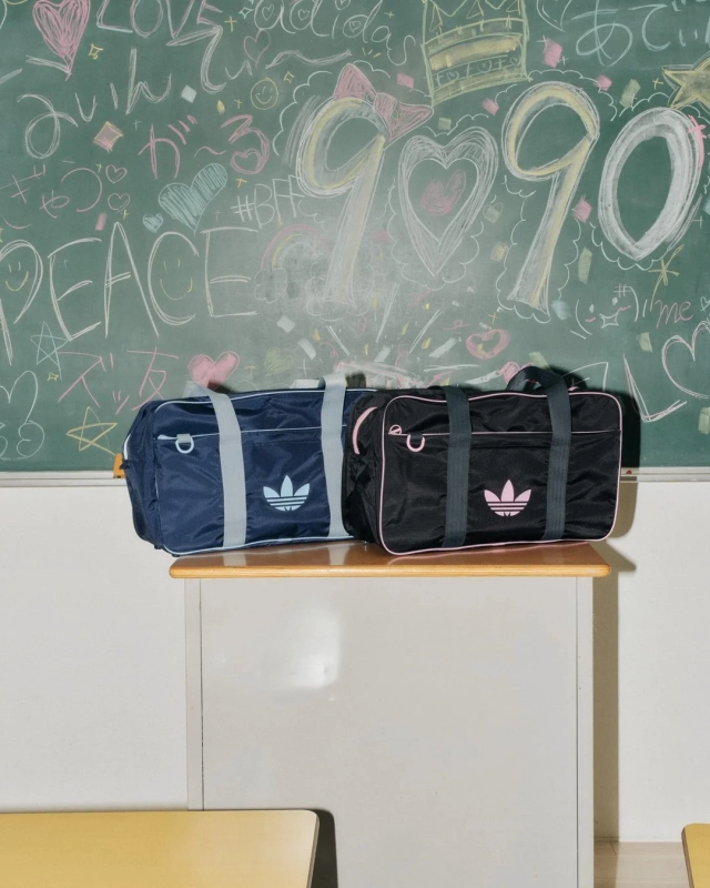 Two adidas schoolbags on a classroom desk, with a blackboard in the background featuring chalk graffiti, capturing a nostalgic student vibe.