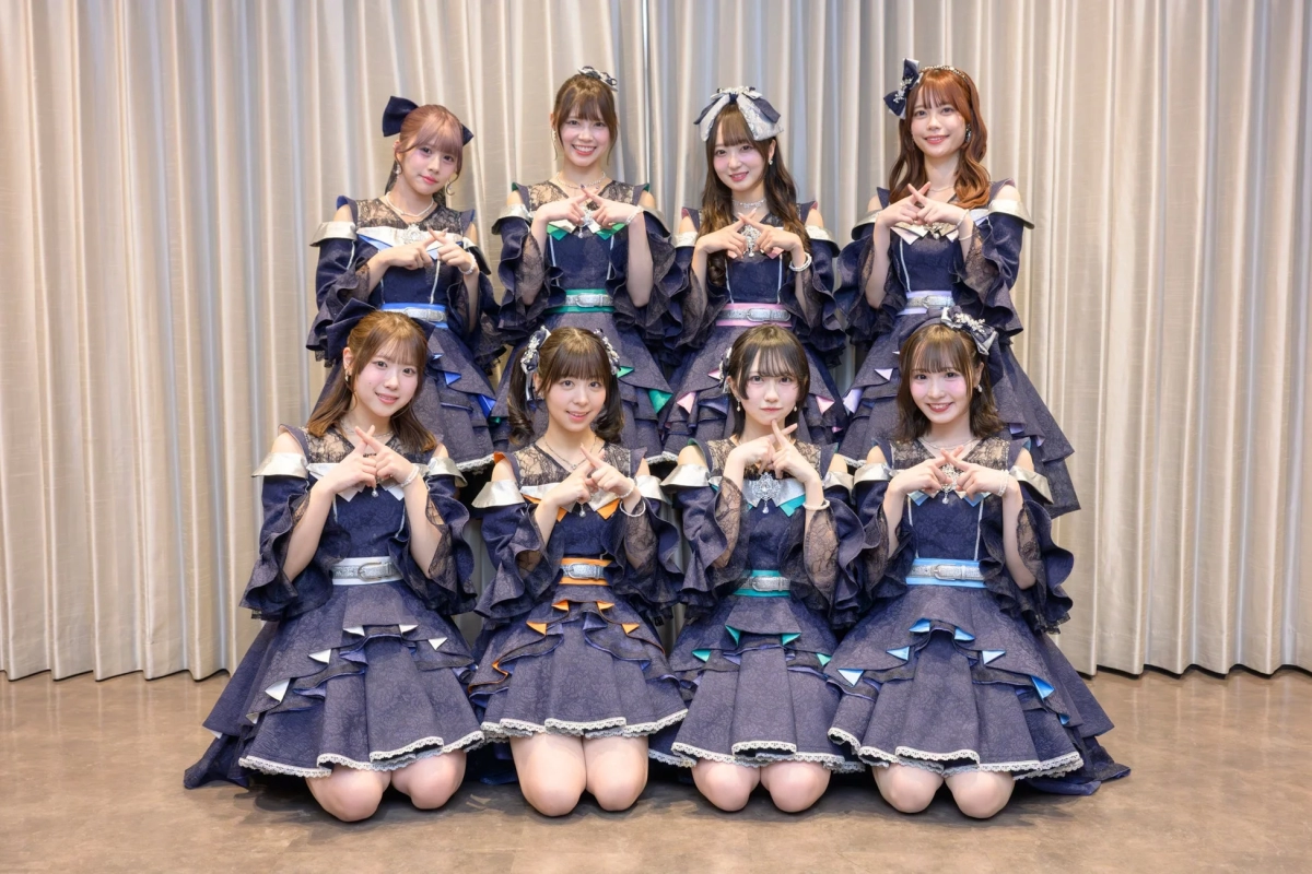 Eight female idol group members posing on stage in matching navy outfits