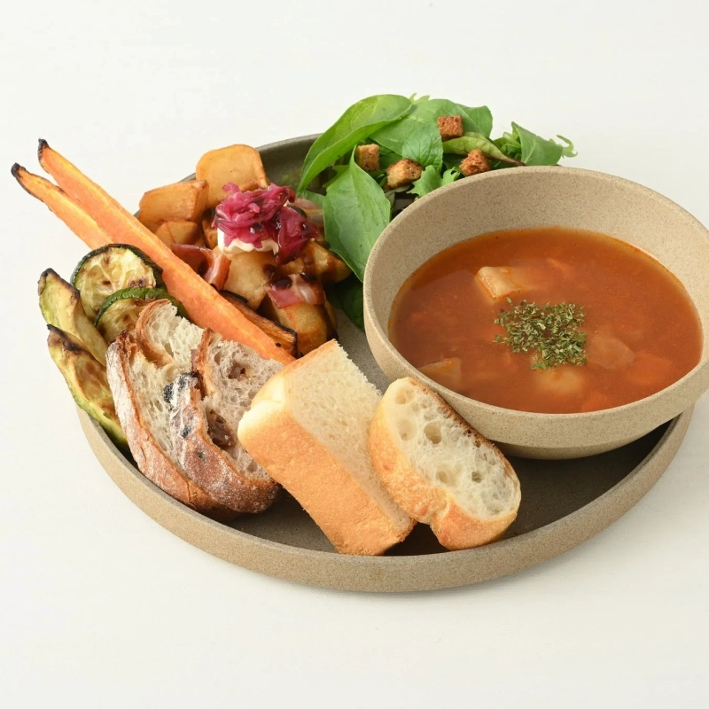 A meal plate with tomato soup, roasted vegetables, French fries, salad, and various breads.