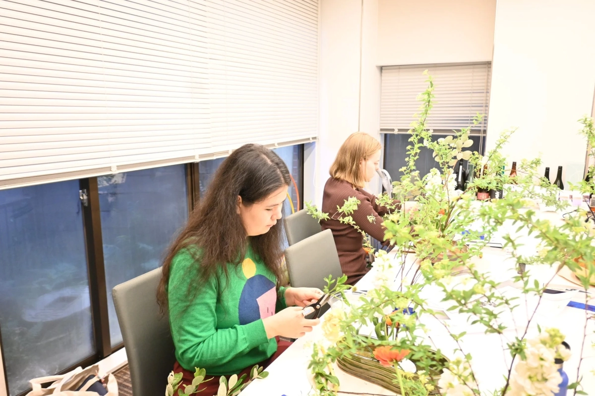Two women participating in an Ikebana workshop, with one woman carefully trimming a plant.