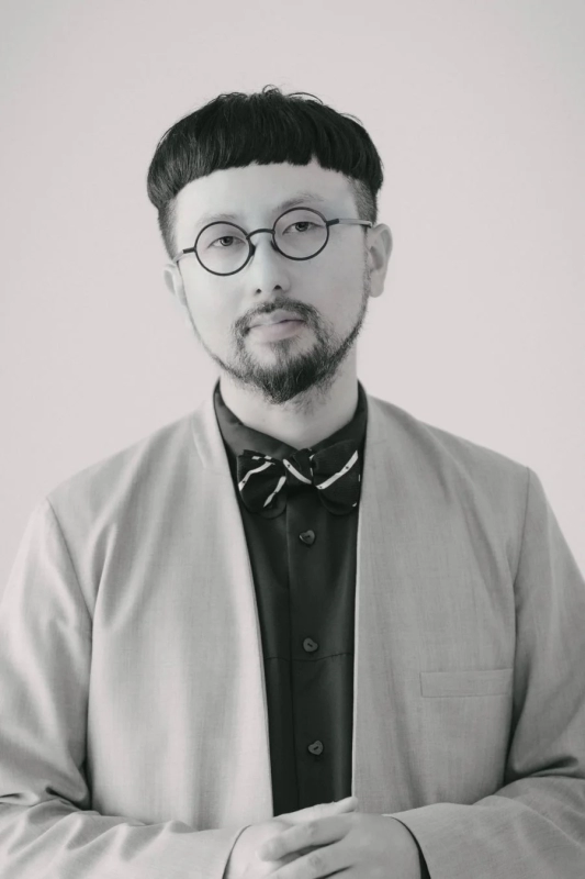 Monochrome portrait of Reiichi Ikeda with round glasses and a bow tie