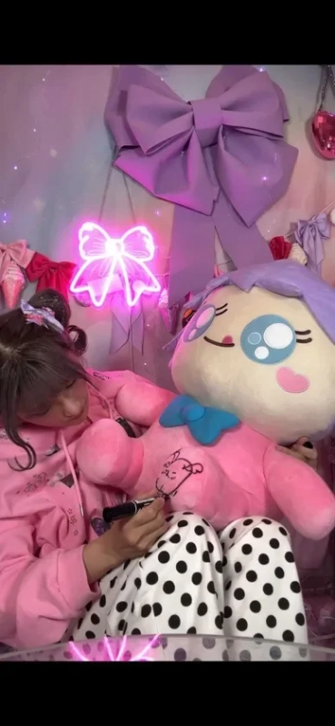 Shinako-chan happily drawing on a giant pink cushion, a campaign prize