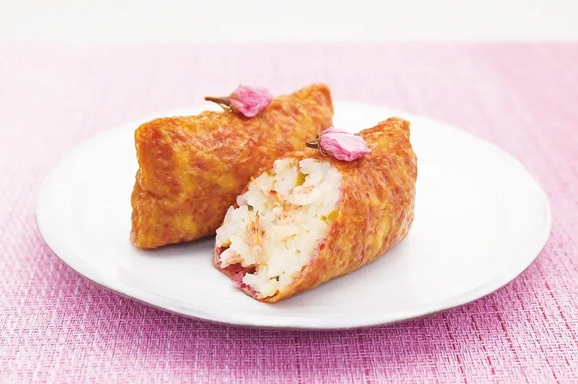 Two inari sushi, one cut open to show sakura shrimp rice