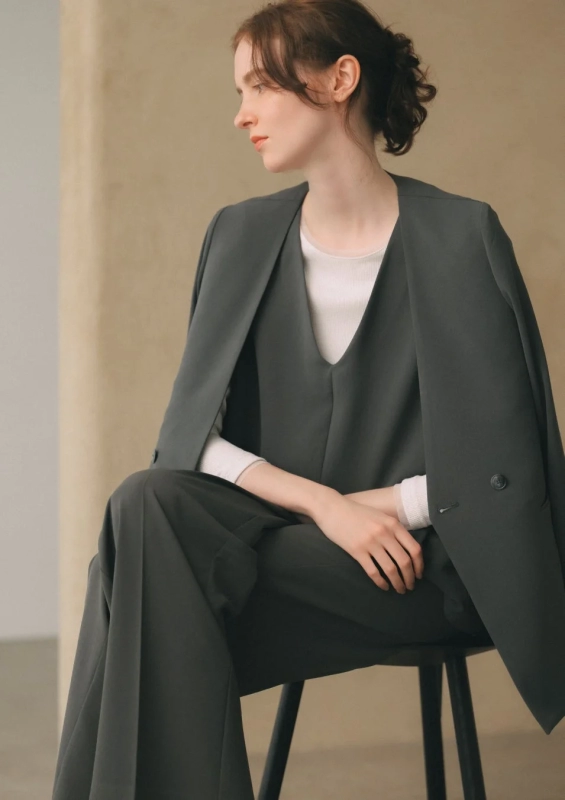 A woman in a dark gray suit set, sitting elegantly, showcasing a sophisticated office style.