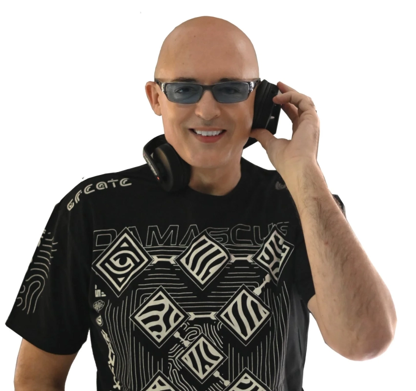 A smiling bald man wearing sunglasses and headphones, dressed in a black t-shirt with text.