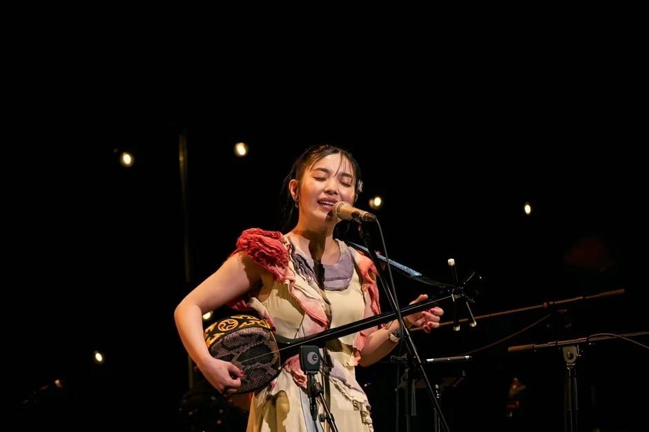Minami Kizuki performing live, playing a traditional string instrument like sanshin