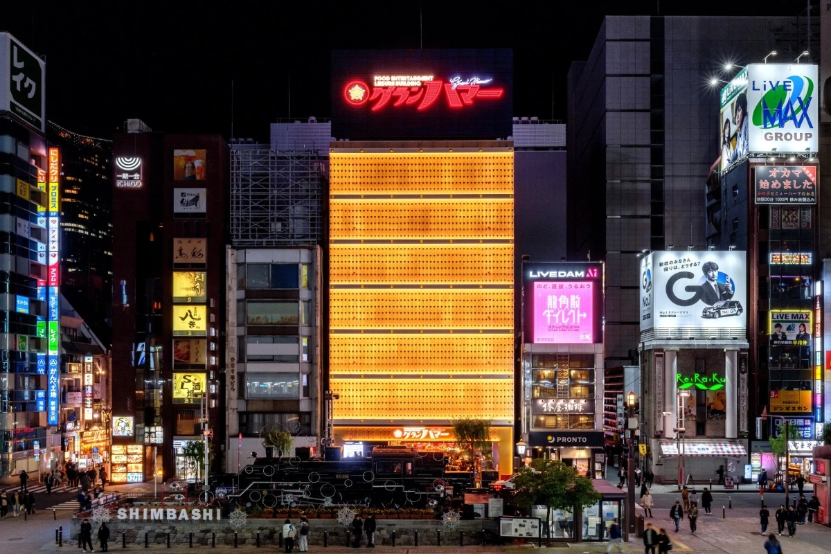 A night view of Shimbashi station area with a steam locomotive and illuminated commercial buildings, including 'Gran Hammer'.