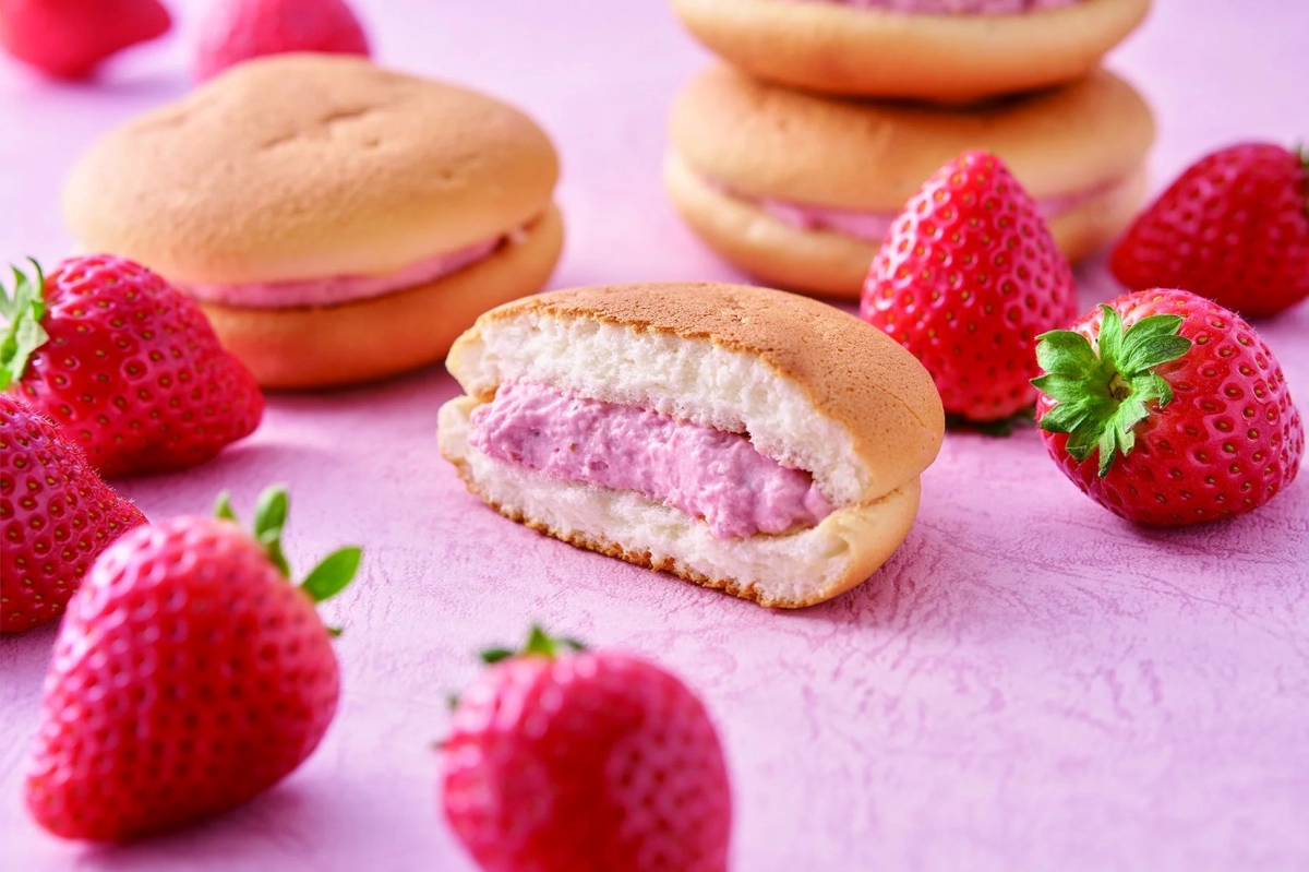 Fluffy pink strawberry cream cake slices and fresh strawberries on a pink background, showcasing a sweet confection.