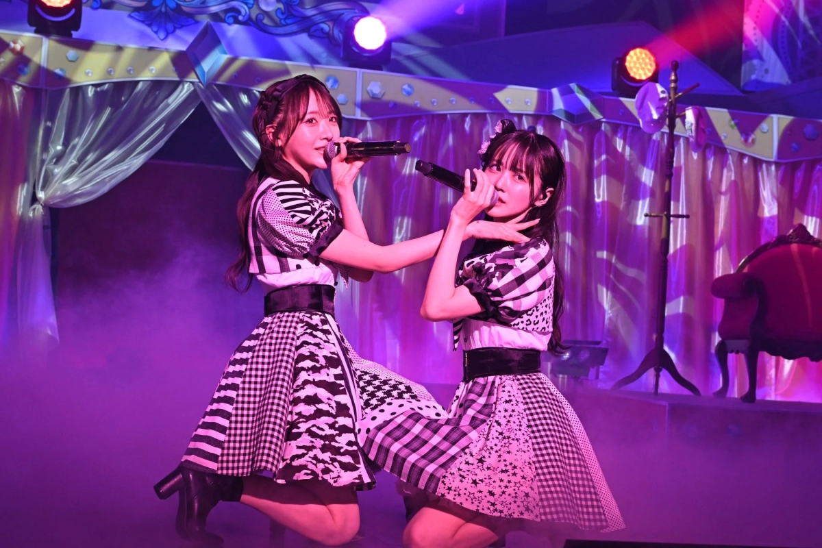Two female idols performing on stage with purple lighting