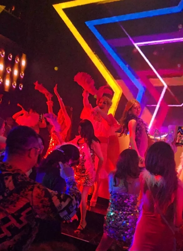 A vibrant club scene with performers, dancers, and a lively crowd enjoying music under colorful neon lights.
