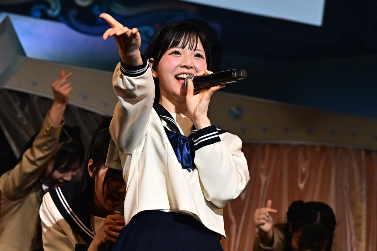 A young female idol in a sailor uniform singing on stage