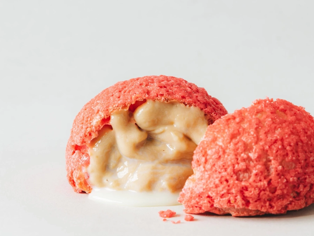 A vibrant red crumble cream puff, cut open to reveal luscious cream.