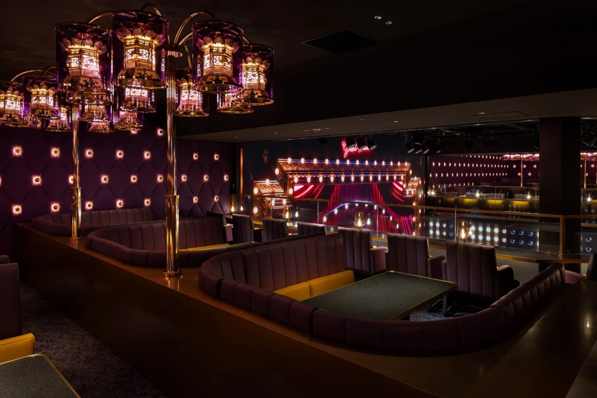 A luxurious lounge interior with purple and gold decor, curved sofas, and a stage with 'Grand' lighting.