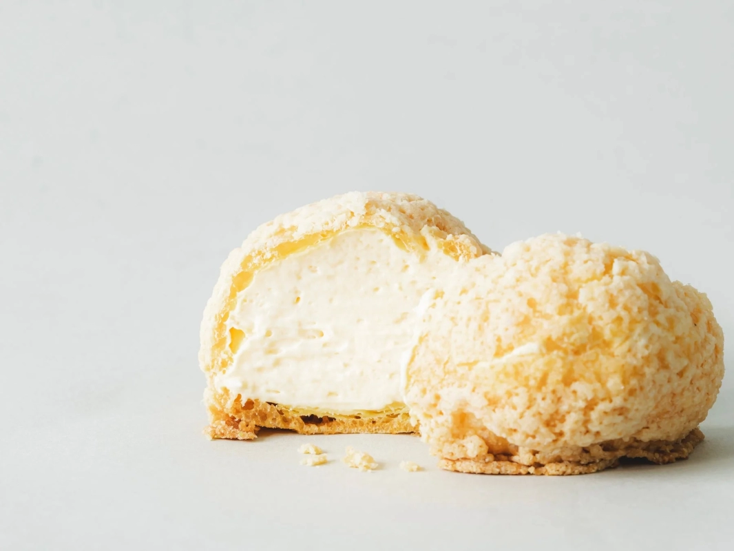 A cookie choux cream puff, cut open to display its generous filling of smooth cream.